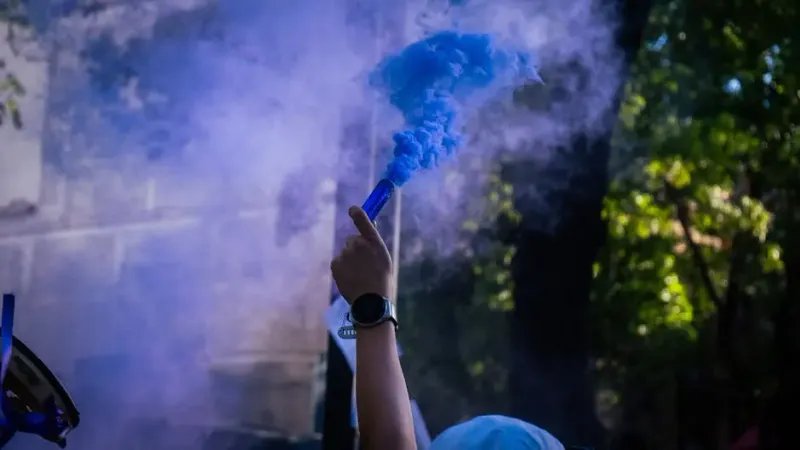 A person holding a blue smoke bomb in their hand